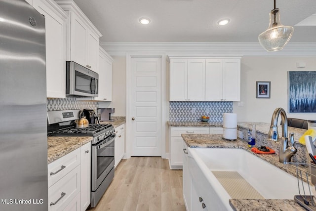 kitchen featuring light wood-style flooring, ornamental molding, stainless steel appliances, white cabinetry, and a sink
