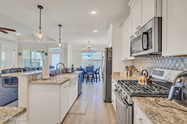 kitchen featuring ornamental molding, stainless steel appliances, ceiling fan with notable chandelier, and open floor plan