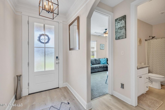 entryway featuring ceiling fan with notable chandelier, baseboards, arched walkways, light wood finished floors, and visible vents