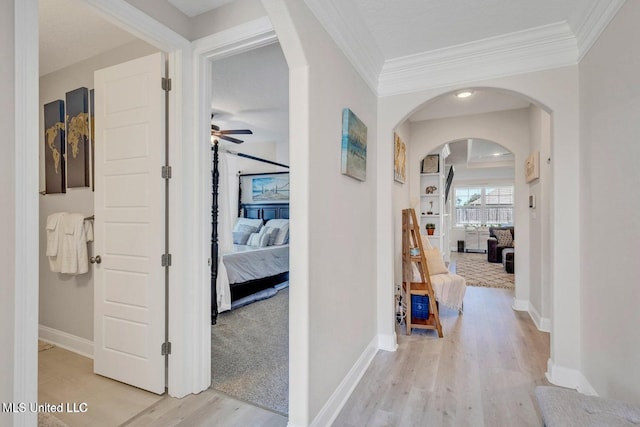corridor featuring ornamental molding, arched walkways, baseboards, and light wood-style floors