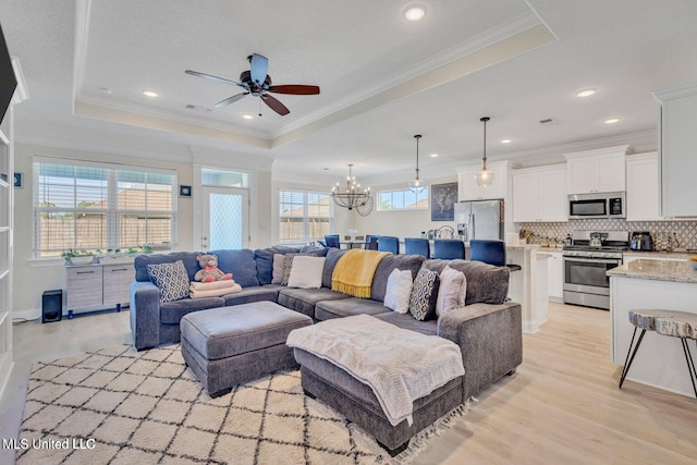 living room featuring a raised ceiling, ornamental molding, ceiling fan with notable chandelier, and light wood-style floors