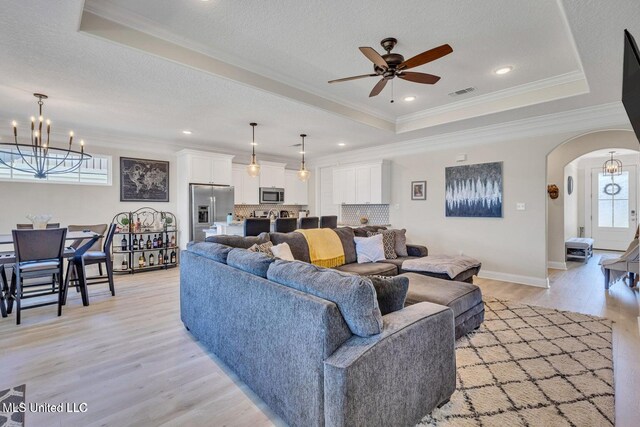 living area featuring a tray ceiling, ceiling fan with notable chandelier, visible vents, and arched walkways