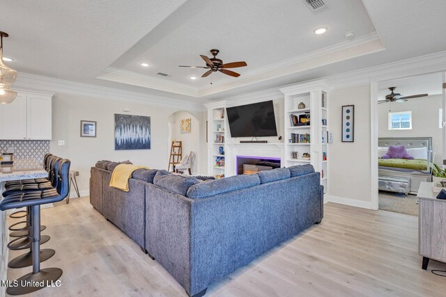 living area featuring light wood-type flooring, a raised ceiling, and ceiling fan