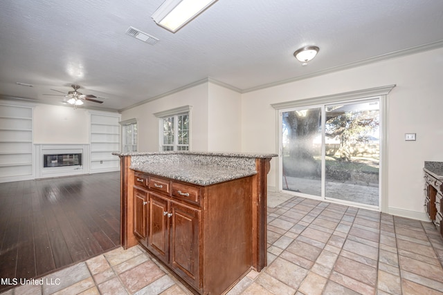 kitchen with a textured ceiling, light hardwood / wood-style flooring, built in features, crown molding, and light stone counters