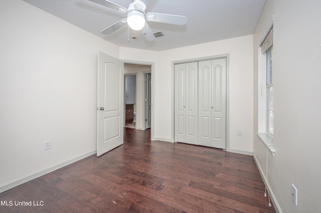 unfurnished bedroom with a closet, ceiling fan, multiple windows, and dark hardwood / wood-style floors