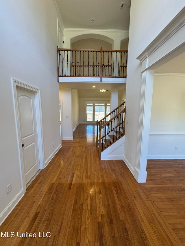 corridor featuring hardwood / wood-style floors, crown molding, and a high ceiling