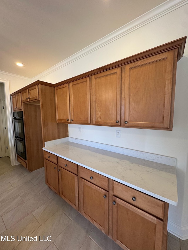 kitchen featuring black double oven, light stone countertops, ornamental molding, and light tile patterned floors