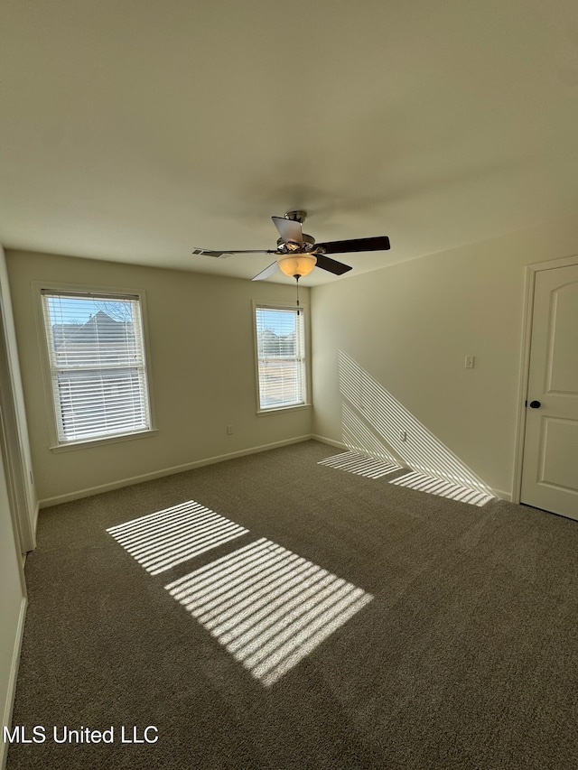 unfurnished room with ceiling fan, a healthy amount of sunlight, and dark colored carpet