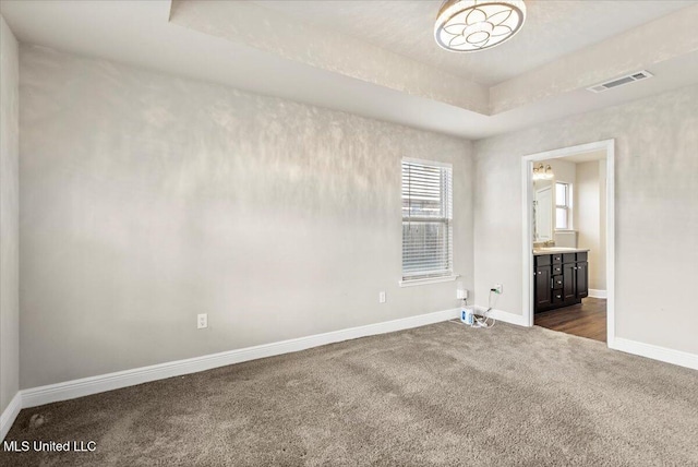 spare room featuring a raised ceiling and dark colored carpet