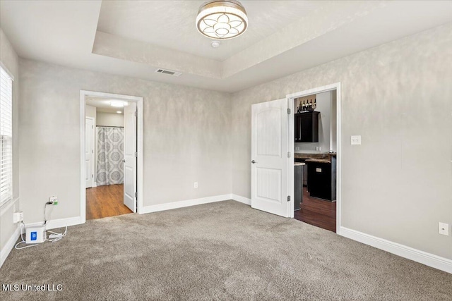 unfurnished bedroom featuring ensuite bathroom, a raised ceiling, and carpet floors