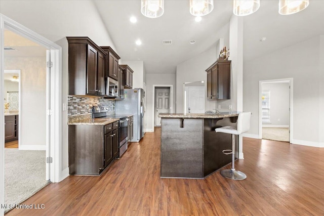 kitchen featuring stainless steel appliances, a breakfast bar area, light stone counters, and decorative light fixtures