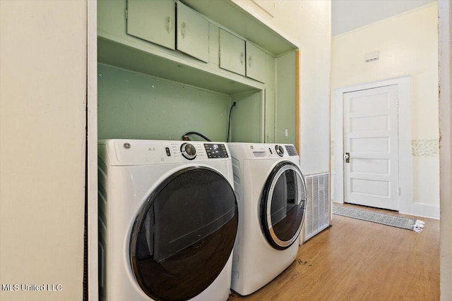 laundry area with cabinets, washer and clothes dryer, and light wood-type flooring