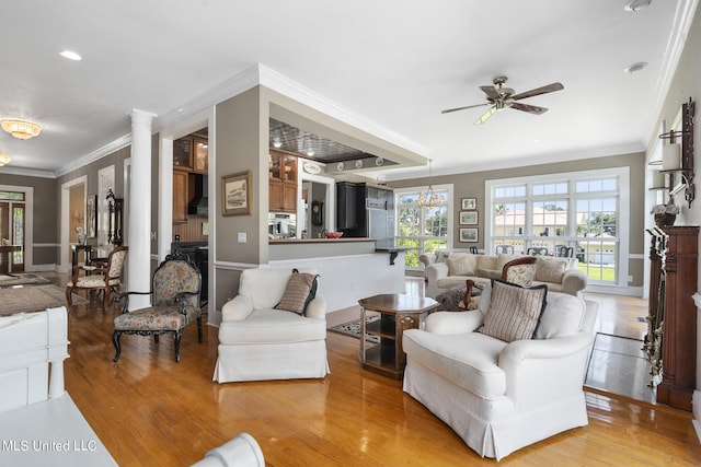 living room with decorative columns, wood-type flooring, ornamental molding, and ceiling fan with notable chandelier