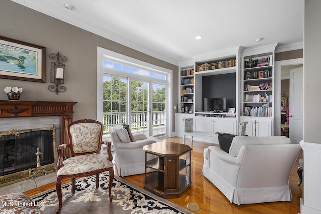 living room featuring built in features, wood-type flooring, ornamental molding, and a fireplace