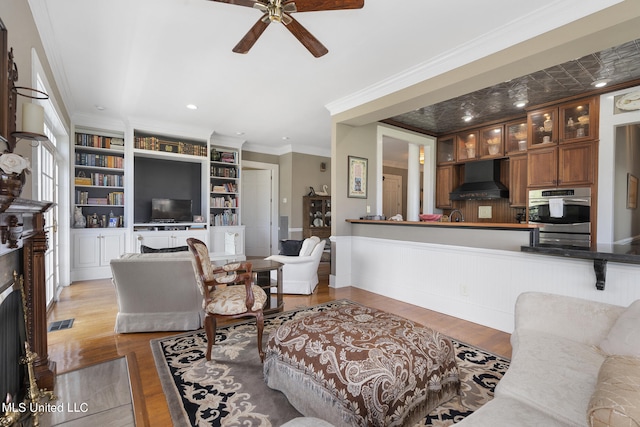 living room featuring light hardwood / wood-style floors, built in features, ornamental molding, and ceiling fan