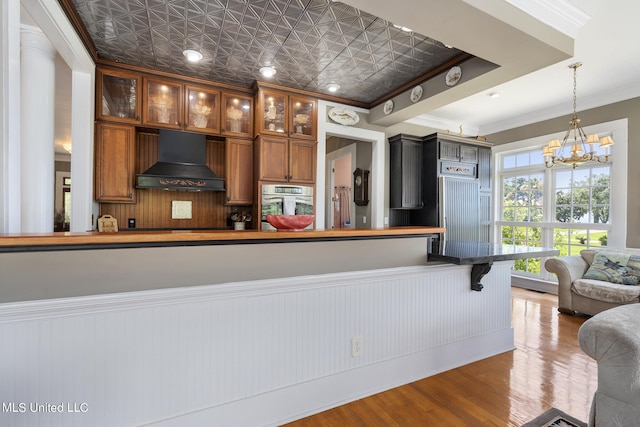 kitchen featuring stainless steel oven, custom range hood, wood-type flooring, ornamental molding, and decorative light fixtures