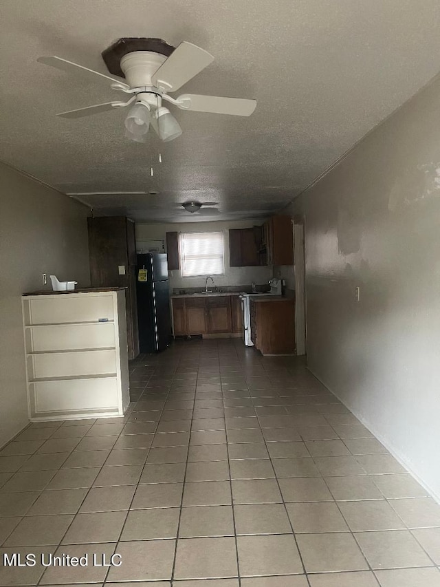 kitchen with white electric range oven, a textured ceiling, light tile patterned floors, and black fridge