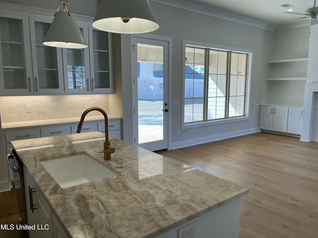 kitchen featuring crown molding, tasteful backsplash, wood finished floors, a sink, and light stone countertops