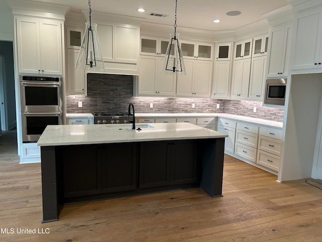 kitchen with an island with sink, stainless steel appliances, light hardwood / wood-style floors, and white cabinets