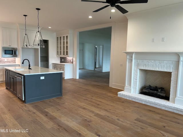 kitchen with white cabinetry, decorative backsplash, stainless steel microwave, and a kitchen island with sink