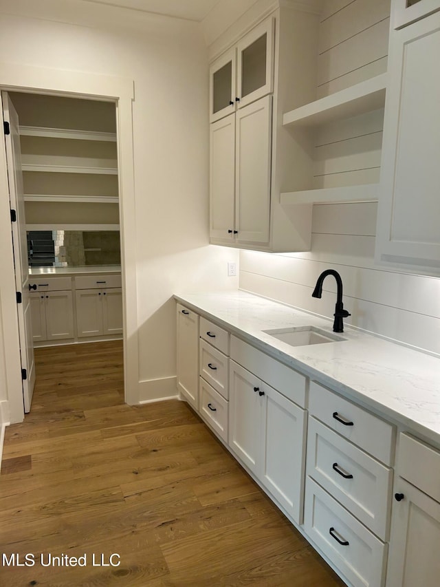 kitchen featuring decorative backsplash, white cabinets, light stone countertops, light hardwood / wood-style floors, and sink