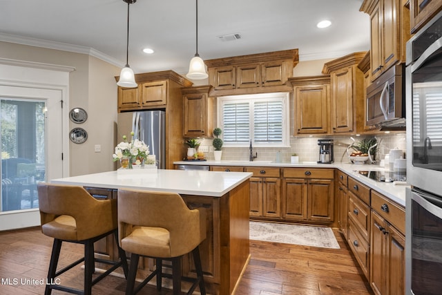 23 Callaway Ct, Hattiesburg, MS 39402 - kitchen with stainless steel appliances, brown cabinetry, ornamental molding, a kitchen bar, and hardwood / wood-style flooring