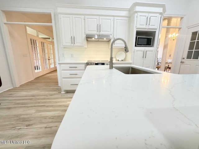 kitchen featuring tasteful backsplash, light stone countertops, stainless steel microwave, and white cabinetry