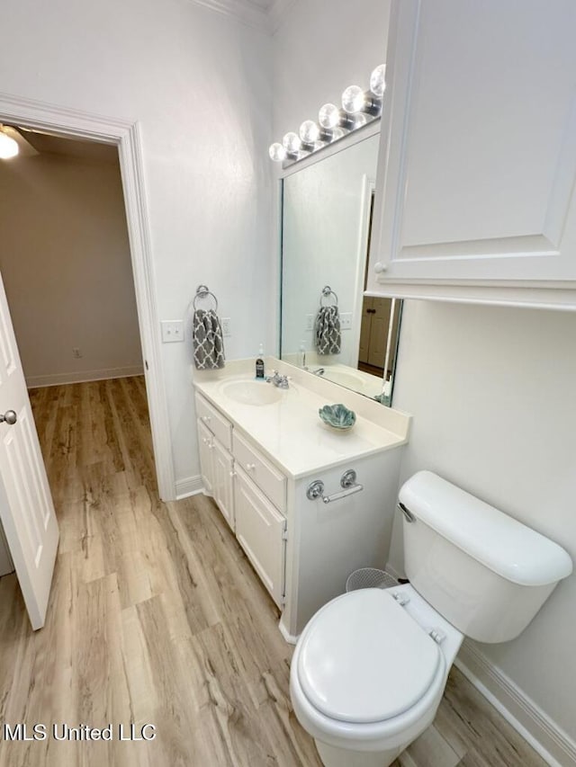 bathroom with toilet, vanity, wood-type flooring, and ornamental molding