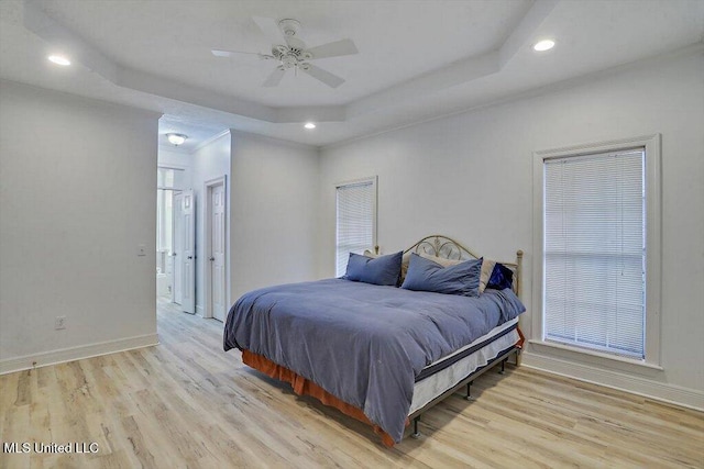 bedroom with light wood-type flooring, ceiling fan, and a tray ceiling