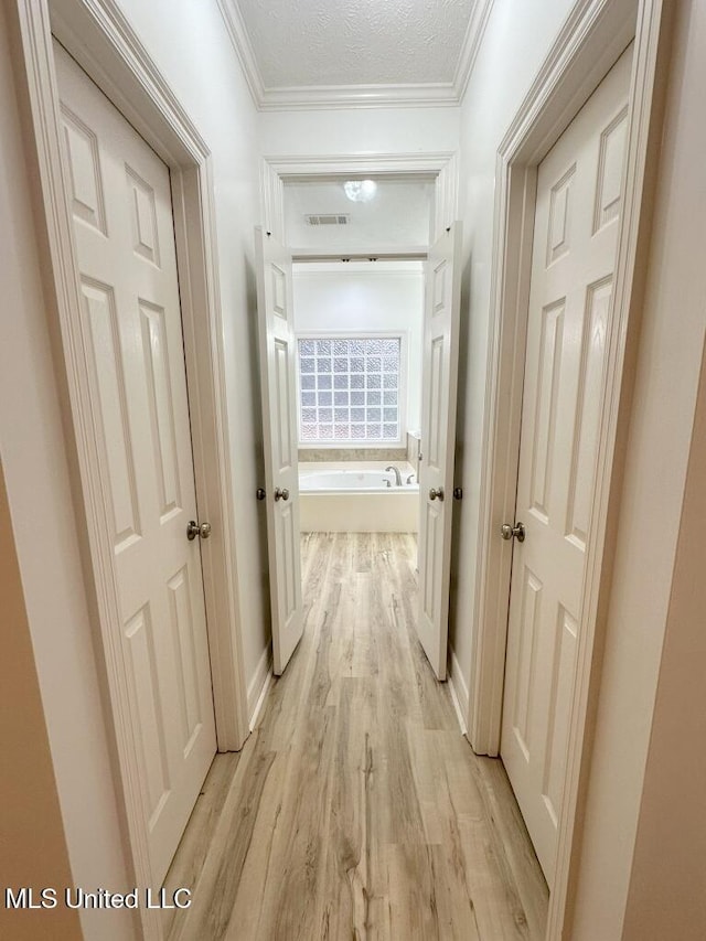 corridor with a textured ceiling, light hardwood / wood-style flooring, and ornamental molding