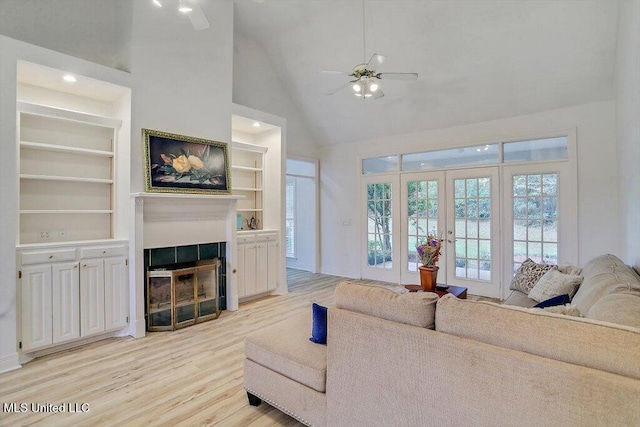 living room with french doors, high vaulted ceiling, a tiled fireplace, ceiling fan, and light hardwood / wood-style flooring