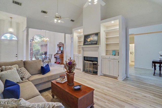 living room with high vaulted ceiling, built in features, light wood-type flooring, and ceiling fan with notable chandelier