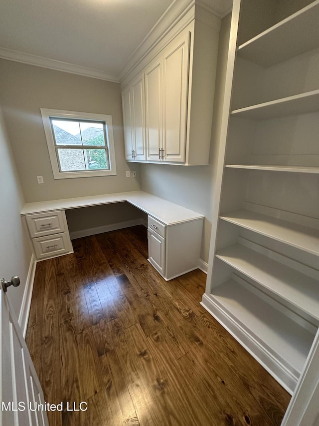 unfurnished office with built in study area, baseboards, ornamental molding, and dark wood finished floors