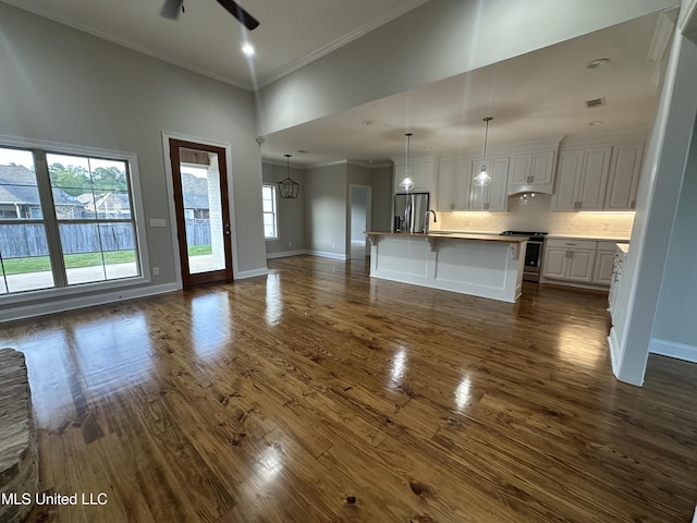 unfurnished living room with a high ceiling, a sink, dark wood finished floors, a ceiling fan, and ornamental molding