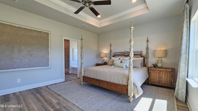 bedroom with ornamental molding, a tray ceiling, ceiling fan, wood-type flooring, and connected bathroom