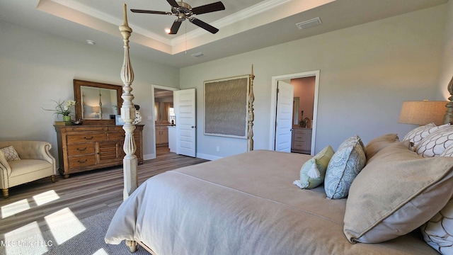 bedroom featuring a raised ceiling, crown molding, ensuite bath, ceiling fan, and dark hardwood / wood-style flooring