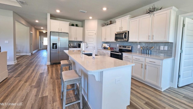 kitchen featuring appliances with stainless steel finishes, dark hardwood / wood-style flooring, sink, a center island with sink, and white cabinetry