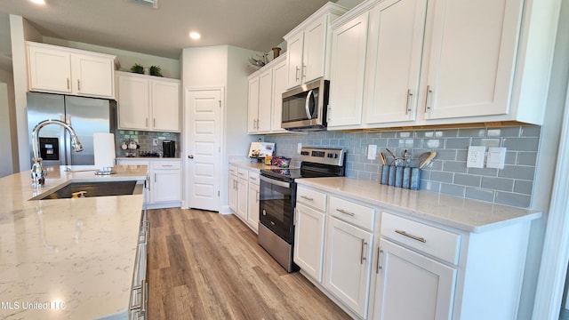 kitchen featuring decorative backsplash, light wood-type flooring, light stone counters, white cabinetry, and stainless steel appliances