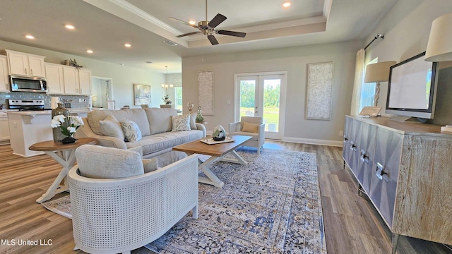 living room with french doors, ceiling fan with notable chandelier, light hardwood / wood-style floors, and a tray ceiling