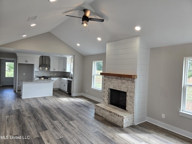 kitchen featuring wall chimney range hood, a sink, lofted ceiling, a ceiling fan, and white cabinetry