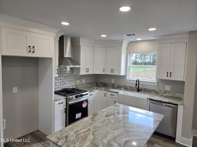 kitchen with wall chimney exhaust hood, stainless steel appliances, white cabinets, a center island, and a sink