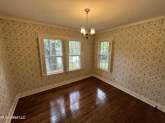 empty room with a notable chandelier, a healthy amount of sunlight, dark wood-type flooring, and crown molding