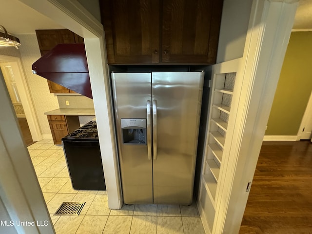 kitchen featuring black stove, stainless steel refrigerator with ice dispenser, light wood-type flooring, and range hood