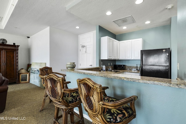 kitchen with dark carpet, white cabinets, black refrigerator, a textured ceiling, and light stone counters