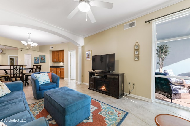 tiled living room featuring ceiling fan with notable chandelier, decorative columns, and crown molding