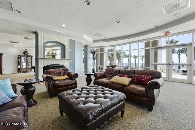 living room with french doors, a textured ceiling, a tray ceiling, a large fireplace, and light colored carpet