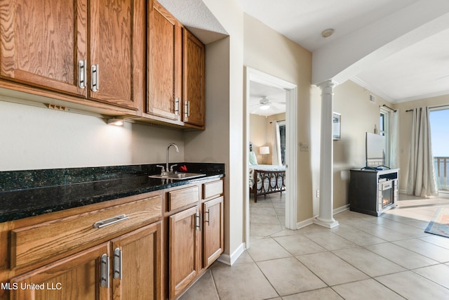 kitchen with ornate columns, sink, dark stone countertops, light tile patterned floors, and ornamental molding