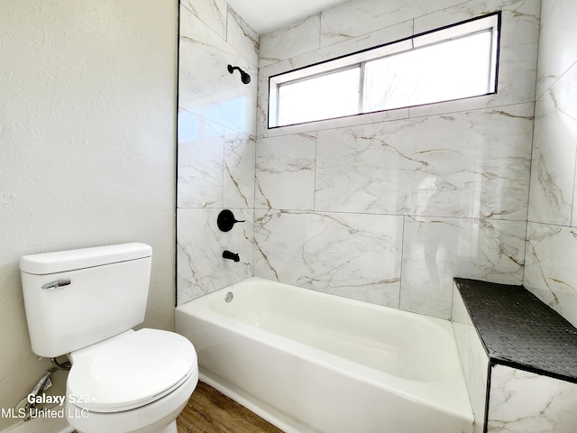 bathroom with tiled shower / bath combo, wood-type flooring, and toilet