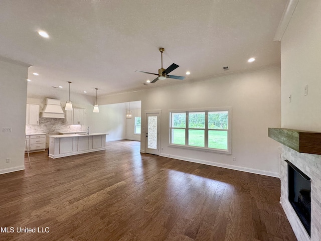 unfurnished living room featuring sink, dark wood-type flooring, ornamental molding, and ceiling fan