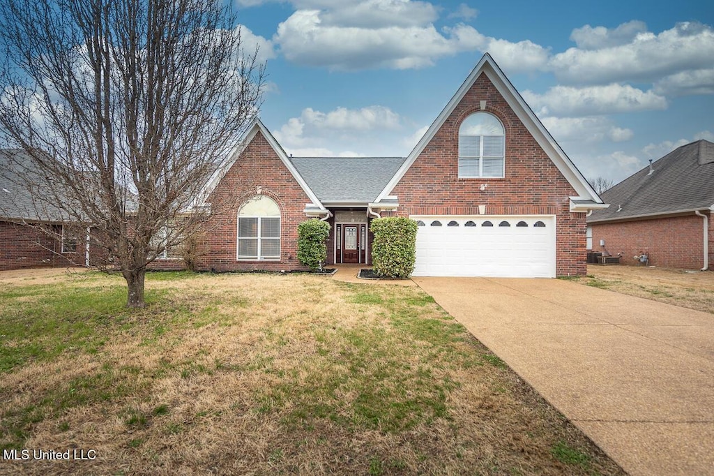 traditional home with a shingled roof, a front yard, brick siding, and driveway